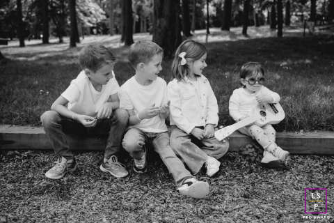 Four young children sit together outdoors as the youngest plays a toy guitar for her amused siblings in Loire, France.