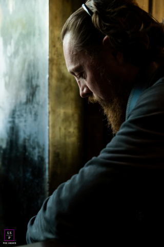 Bearded Man Sits Thoughtfully Beside Window In Soft Light In Indre A bearded man sits quietly beside a window, his thoughtful expression illuminated by soft natural light in Indre, France.
