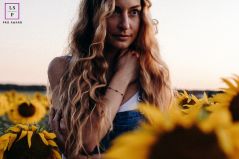 Woman Stands Among Blooming Sunflowers In Evening Light In Indre France A woman stands among blooming sunflowers, framed by golden petals and soft evening light in the countryside of Indre, France.