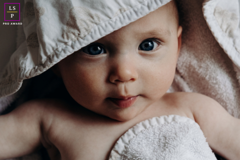 Baby Girl Wrapped In Soft Towels After Bath Time In Indre A baby girl gazes toward the camera while wrapped in soft towels after bath time at home in Indre, France.