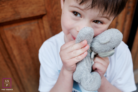 A young boy cuddles his favorite teddy bear close to his face while smiling softly during a playful day in Paris.