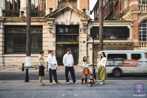 A family stands together along a city street as a passing vehicle adds movement and energy to the urban scene in Guangzhou.
