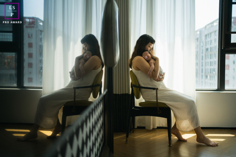 A mother cradles her newborn beside a mirror, creating a layered reflection of their quiet connection inside a home in Chengdu.