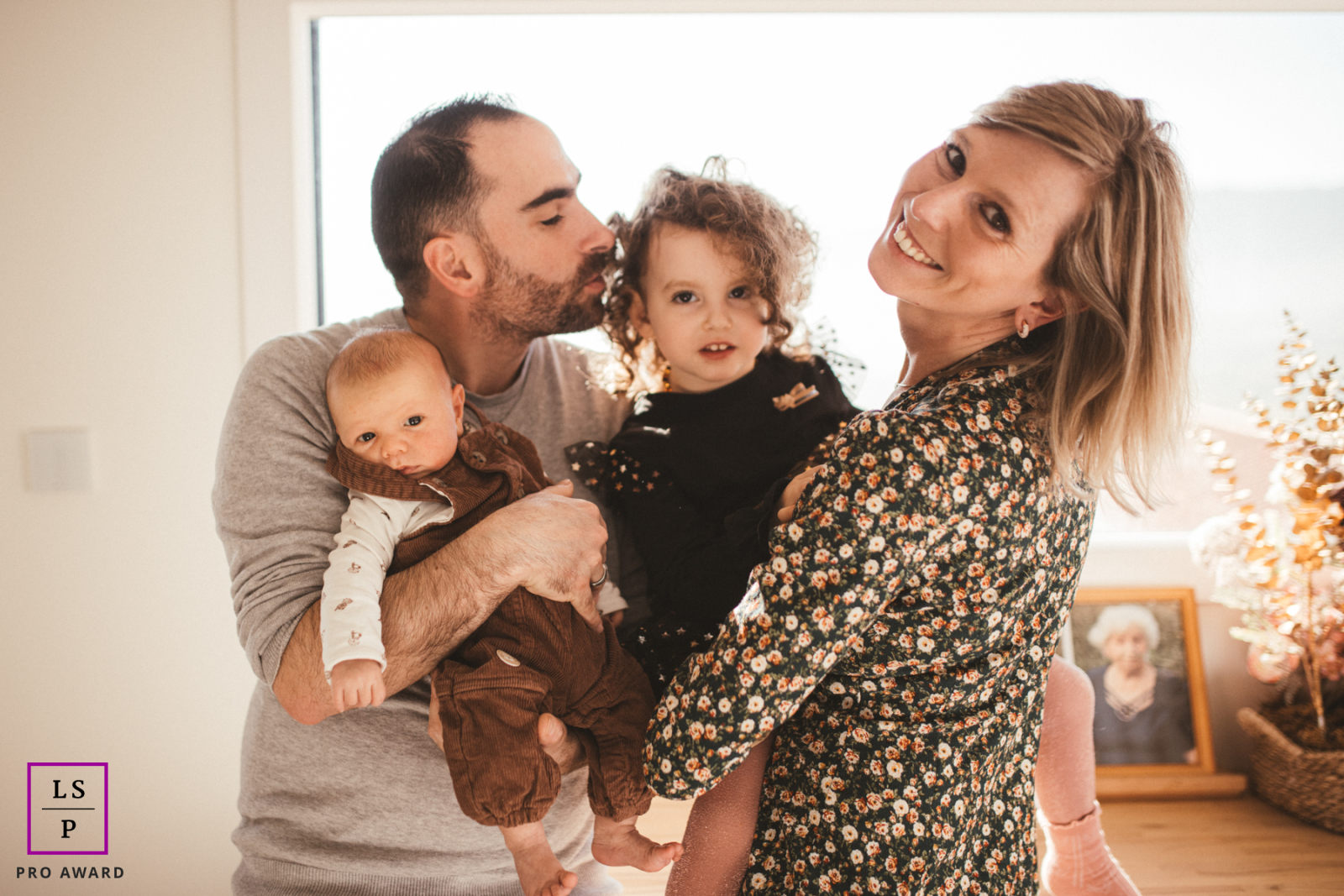 In Saint Martin la Plaine, Loire, a family shares a heartfelt moment at home in their living room. Mom and dad hold their two young kids, radiating happiness and unity.