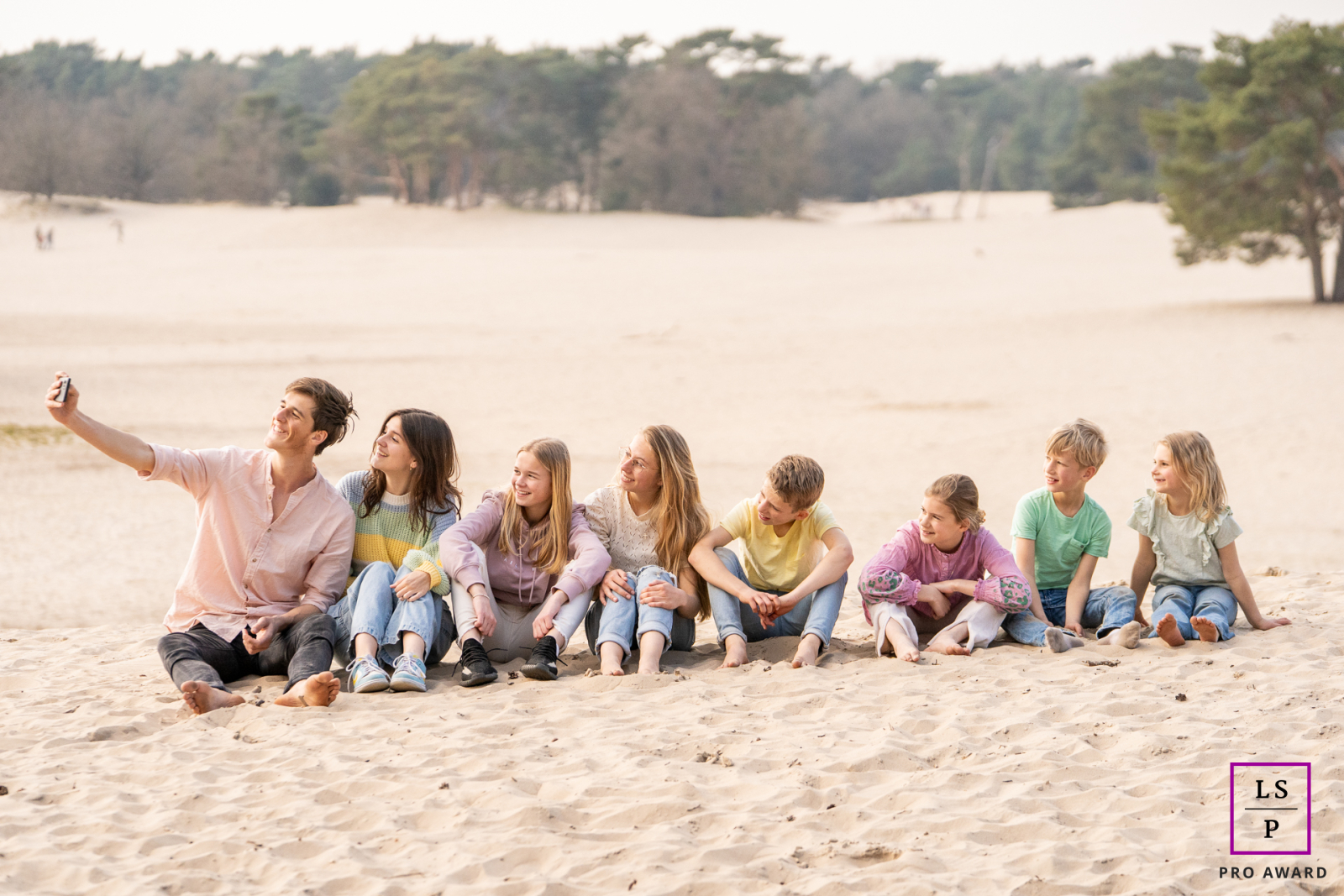Across the sandy landscape of Soesterduinen, cousins pause for the inevitable selfie. The relaxed spacing, soft light, and wandering gazes give the photograph humor and effortless authenticity.