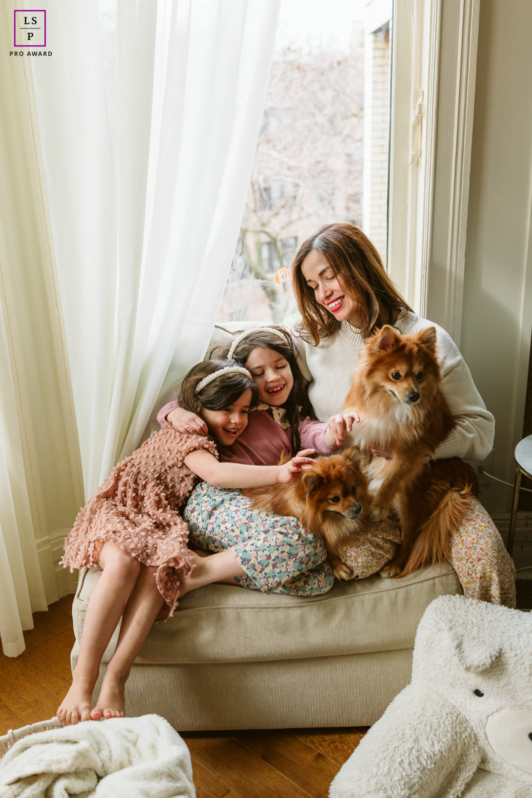 Morning light pours through the Chicago window as laughter collapses this family into one joyful tangle of blankets, children, and remarkably patient dog.