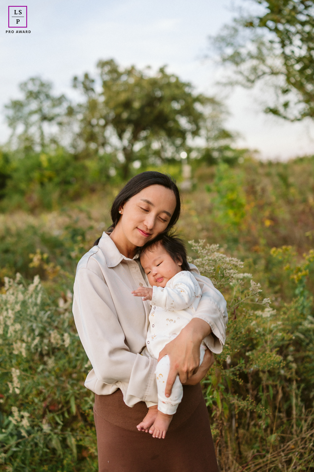 In Chicago, Illinois, the mother cradles her baby gently among the tall grasses, both resting peacefully with eyes closed. The soft natural light and quiet setting give the portrait tenderness, stillness, and the fleeting beauty of early motherhood.