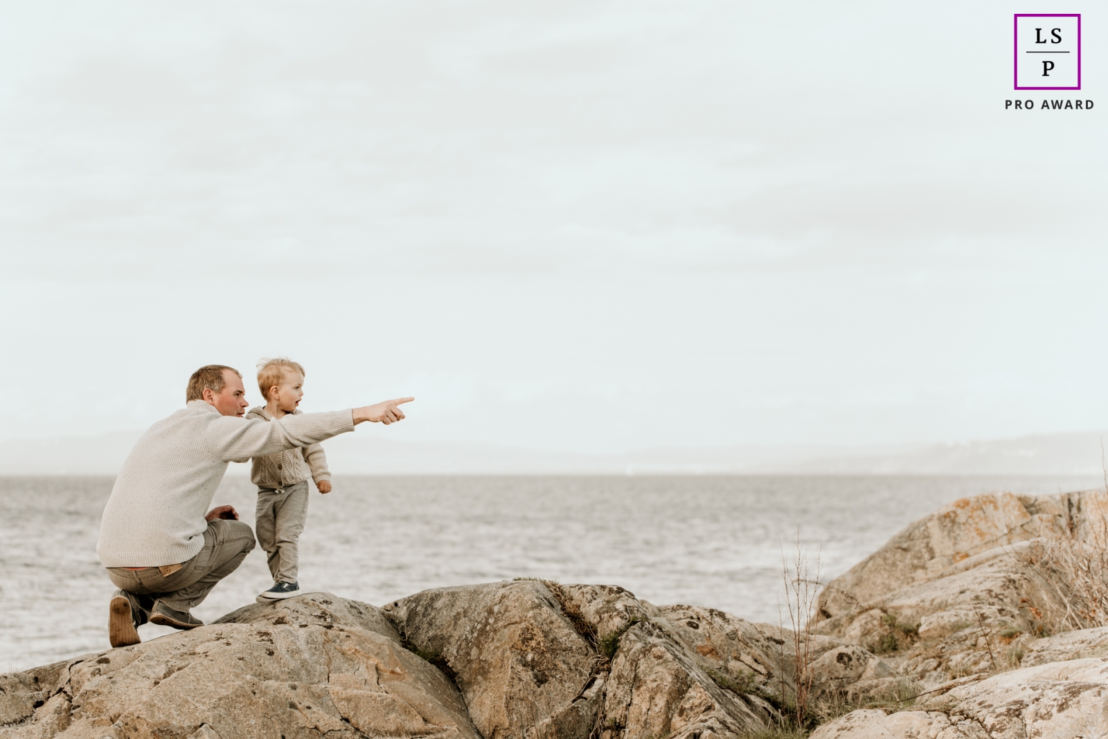 An Oslo father is on the beach rocks and pointing at something his son should see at the ocean of Norway