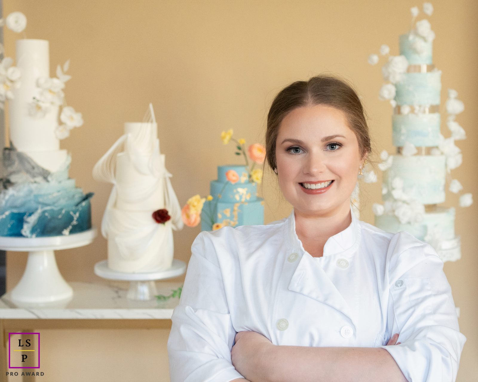 A baker from Hanami Cake Design in Maine, New England, stands smiling warmly in front of a table displaying her cakes. The scene features a soft color palette and inviting atmosphere.