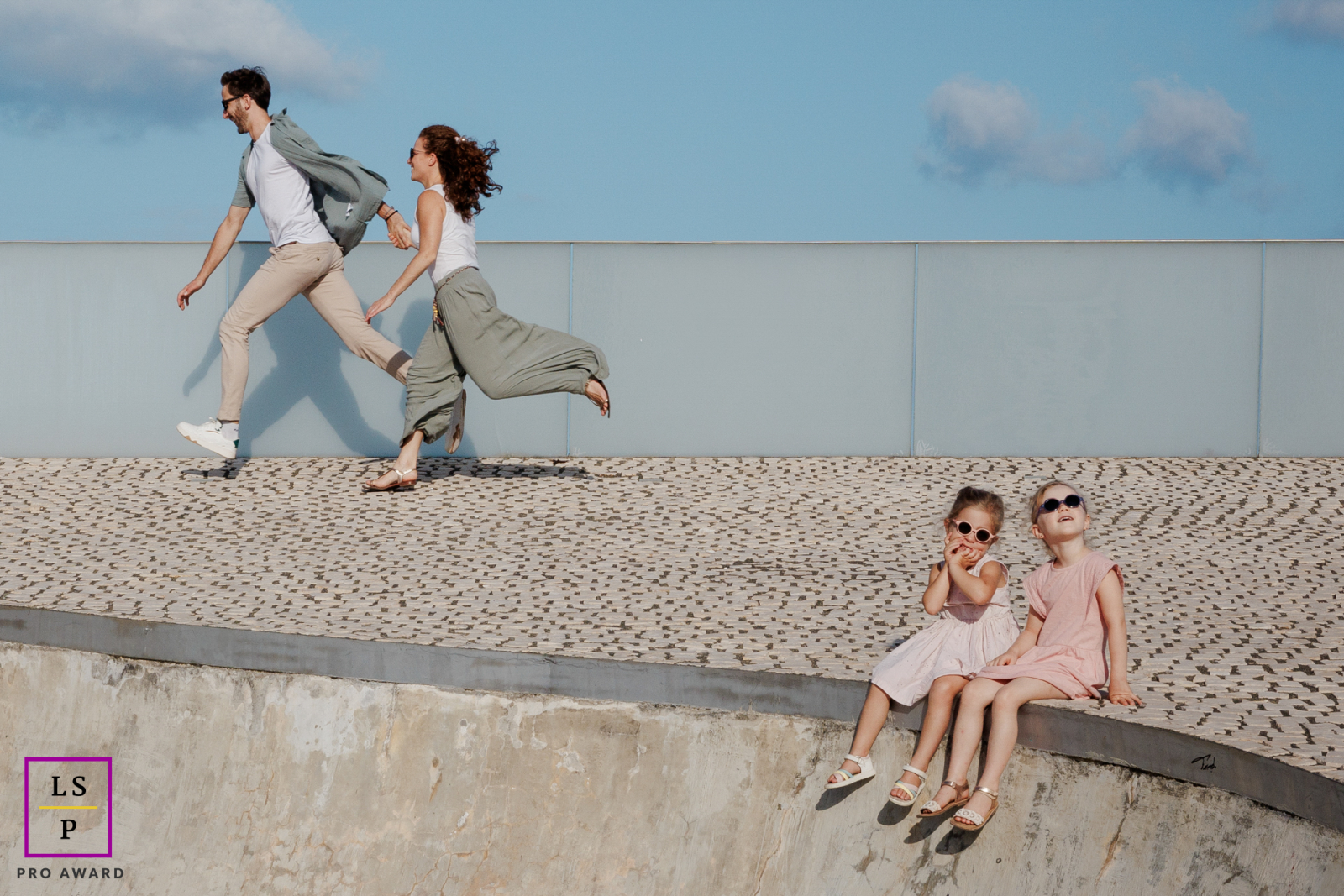 In Paris, the parents appear to drift out of the frame while their daughters sit calmly below, almost unimpressed by the escape. The unusual spacing and playful imbalance turn this family portrait into something humorous and wonderfully unexpected.