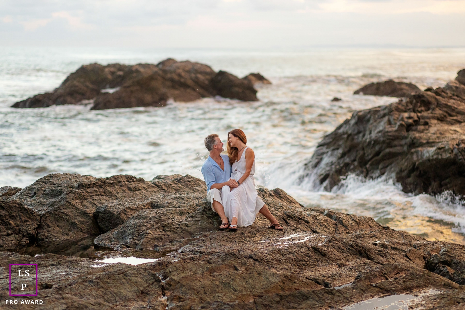 This is a lifestyle image on a beach in Costa Rica with the couple sitting on the rocks with the crashing waves behind them