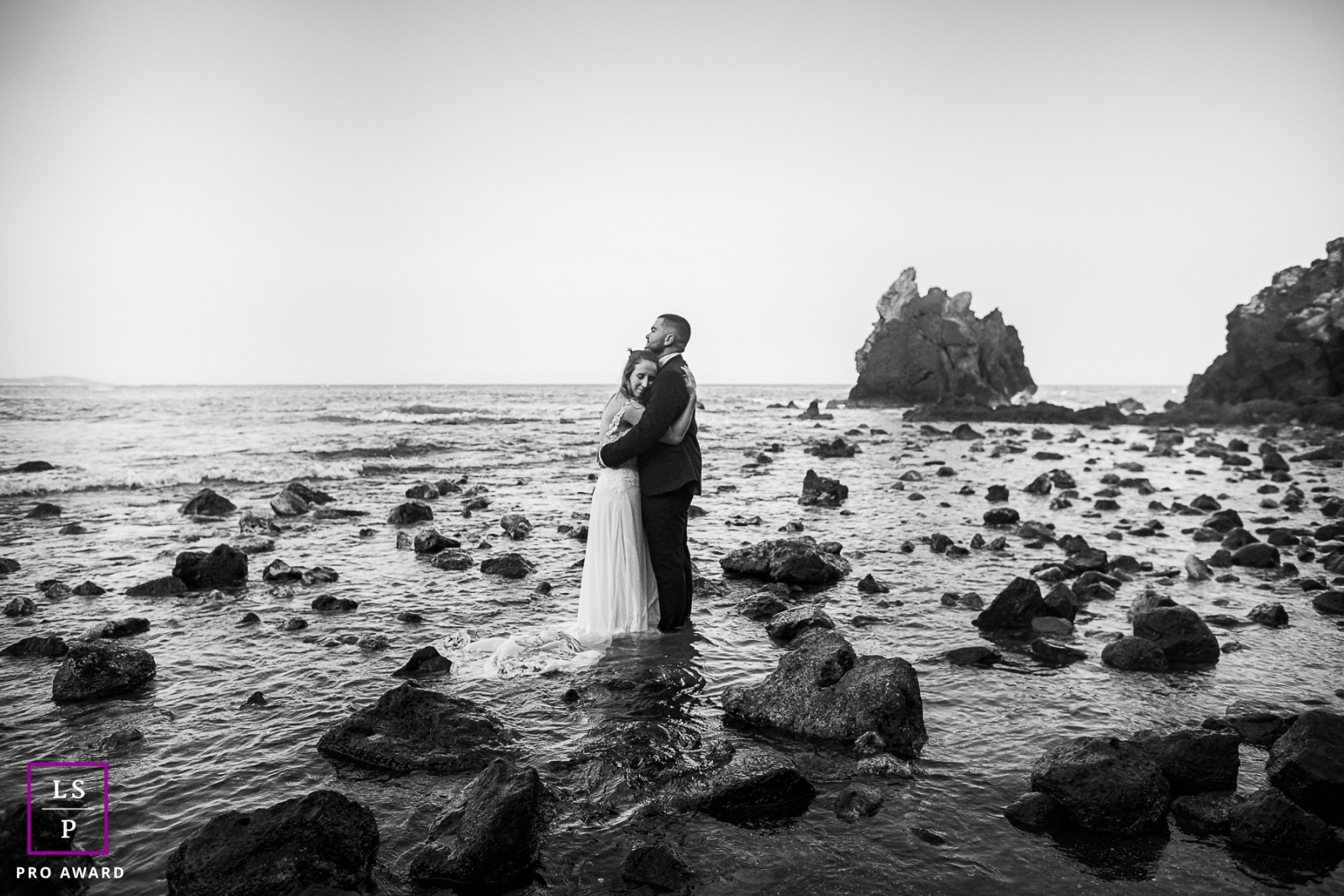 Dans l'Hérault, une photographie en noir et blanc capture un couple le jour de leur mariage, debout au milieu de rochers accidentés, créant une scène intemporelle et romantique.
