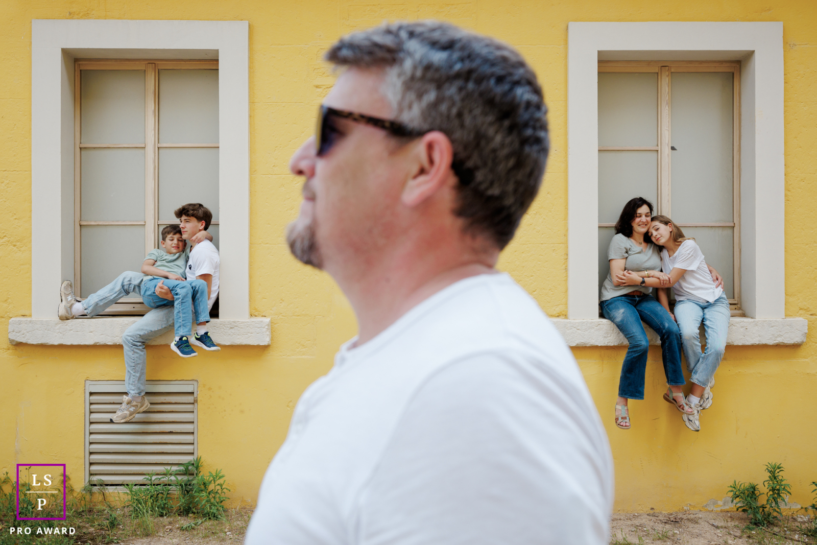 In Paris, a family portrait features dad in the foreground in profile, while the rest of the family sits on window sills behind him. The composition highlights familial connection with a stylish, layered arrangement.