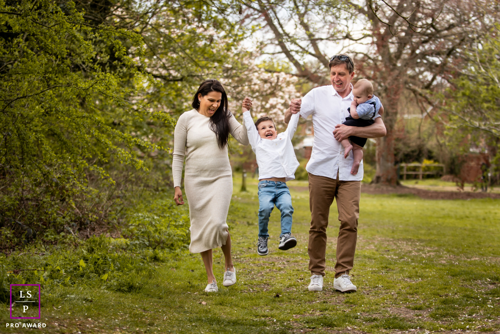 Among the spring blossoms in St Albans, this family moves through the park with playful energy as their young son swings happily between his parents. The soft greenery and relaxed movement give the photograph warmth, lightness, and natural connection.
