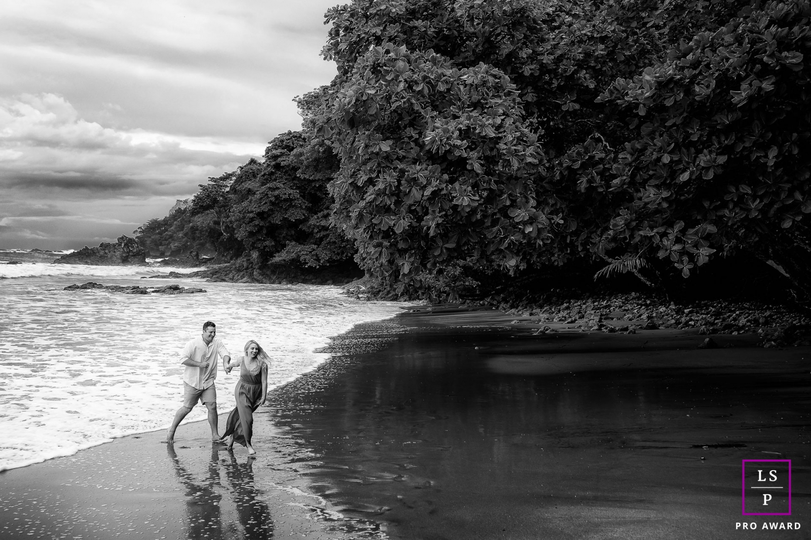 This is a lifestyle photo from Costa Rica in BW of the couple running away from the waves on the sand