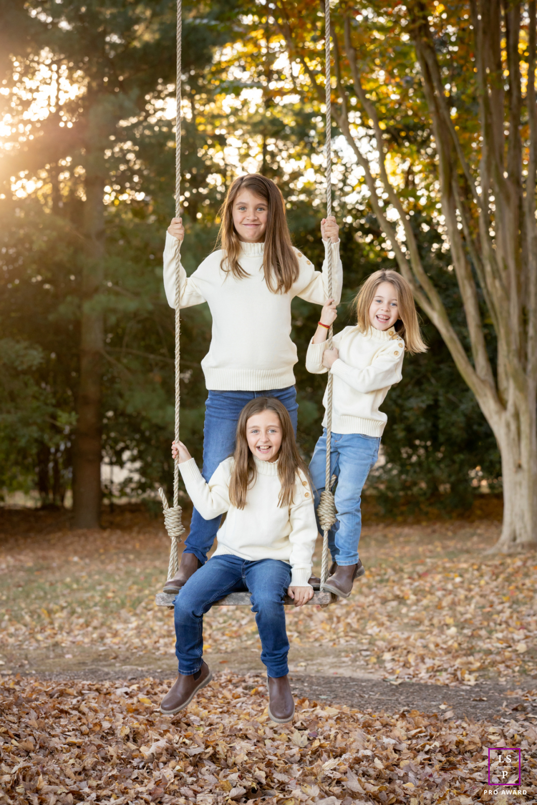 In St. Michaels, Maryland, three girls smile and pose while sitting together on a rope and wood plank swing hanging from a large tree, all looking warmly at the camera.