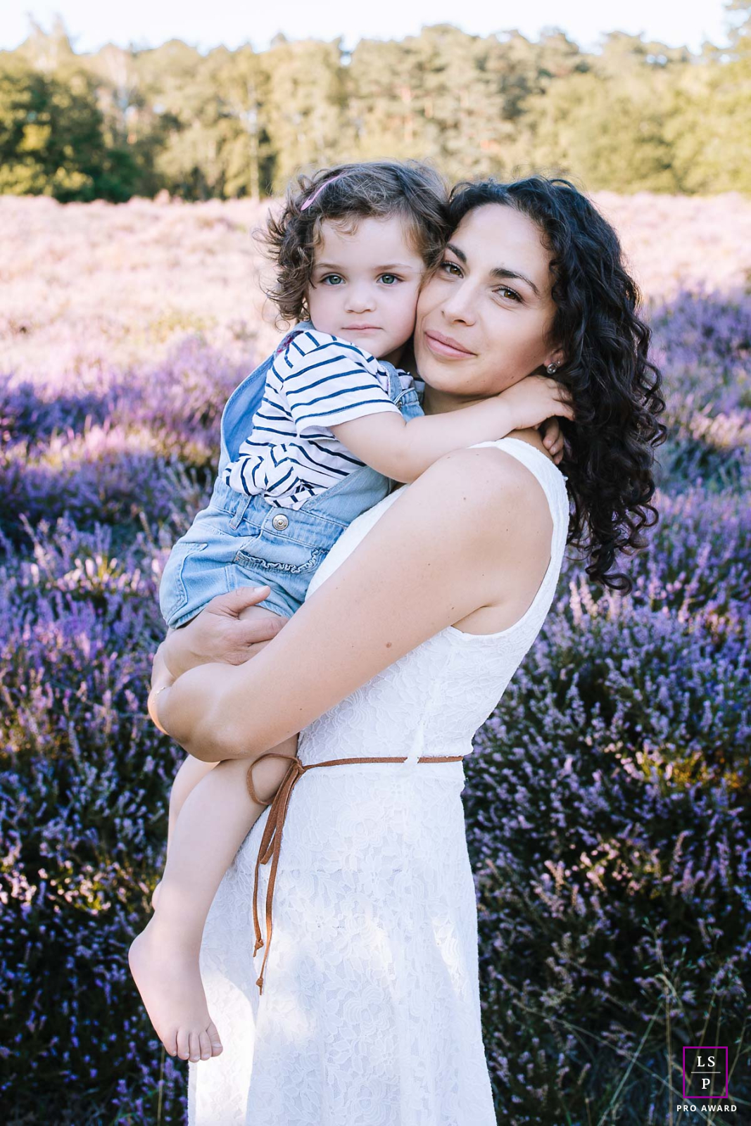The purple heather provides a painterly backdrop, yet it is that firm, tiny grip on the shoulder that steals the show. A masterfully captured study in maternal strength and childhood trust.