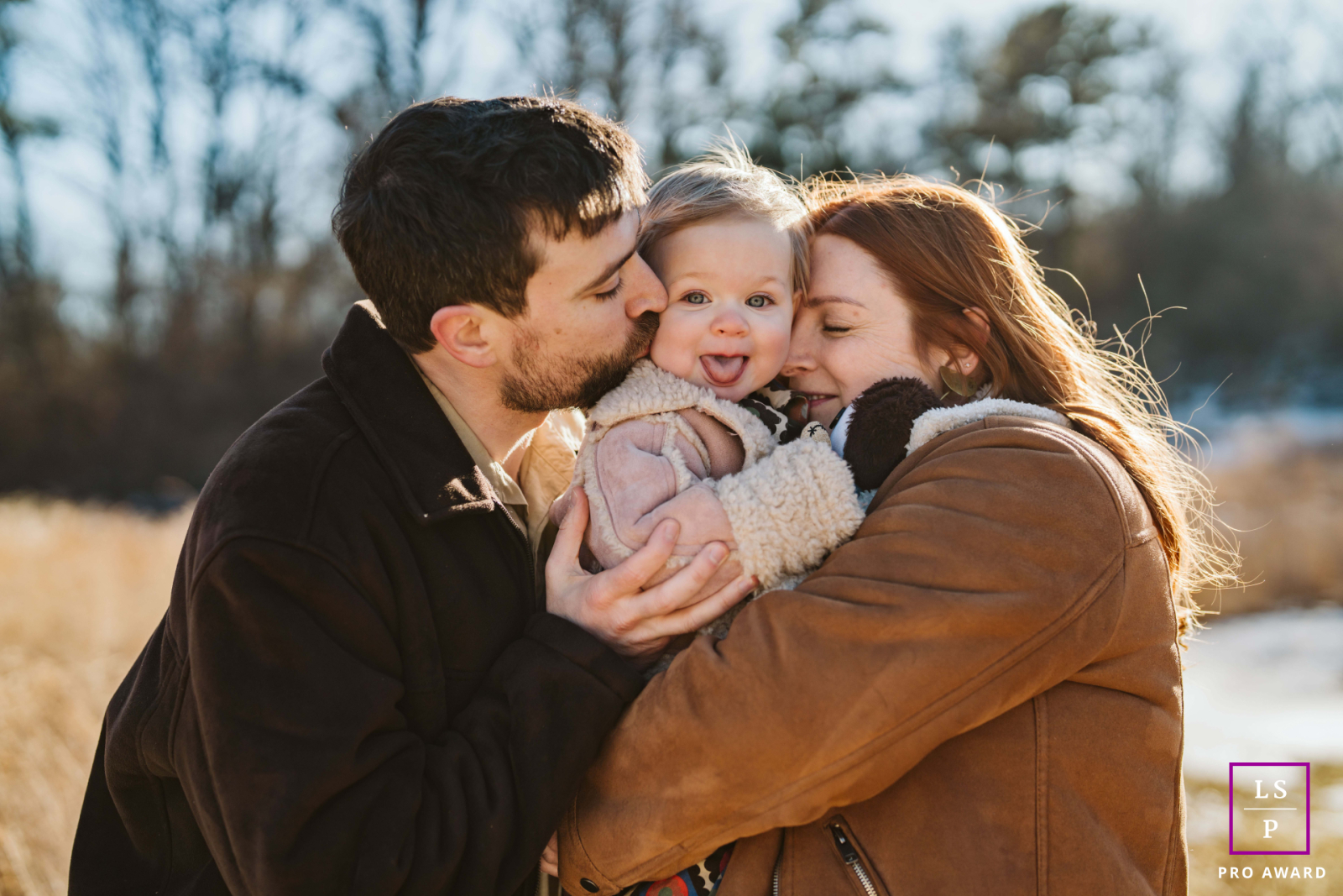 In Clinton Township, this joyful child sits between two kisses, completely surrounded by affection and winter light. The tight composition and warm tones make the photograph feel intimate, playful, and deeply loved.