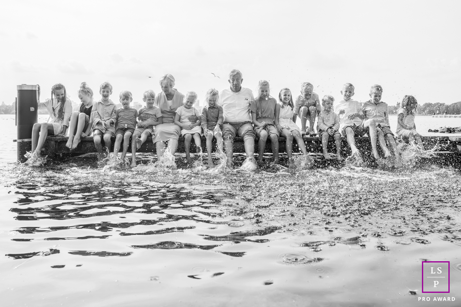 At Kralingse Plas in Rotterdam, grandparents sit surrounded by fourteen grandchildren, all gleefully kicking water like a beautifully coordinated act of chaos. The black and white simplifies the busy scene, allowing laughter and family connection.