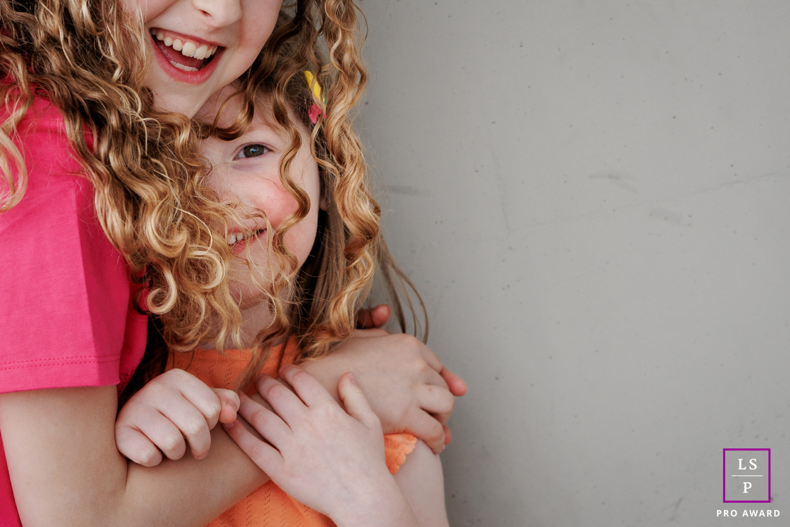 In Paris, the older sister wraps herself protectively around the younger as both dissolve into laughter and closeness. The tight crop and soft expressions remove every distraction, leaving a portrait filled entirely with affection and sibling connection.