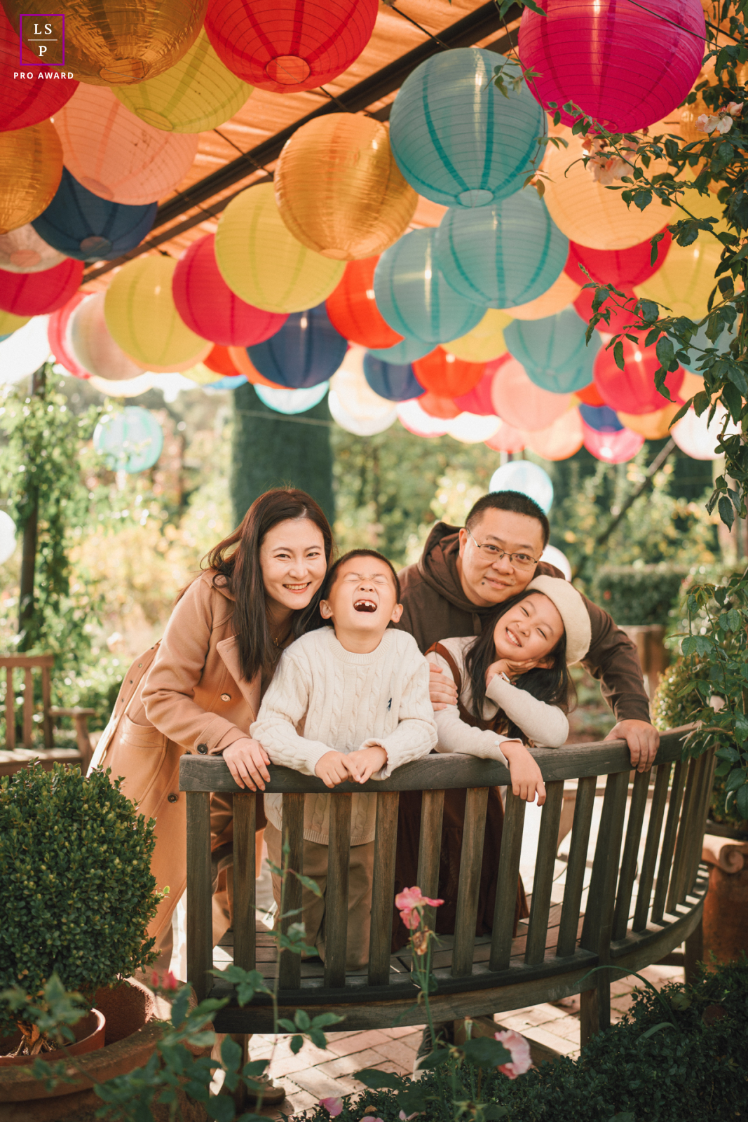 At Filoli, the family gathers beneath colorful lanterns as laughter spills naturally across the frame. The vibrant overhead decorations and warm garden light give the portrait joy, closeness, and a festive sense of togetherness.