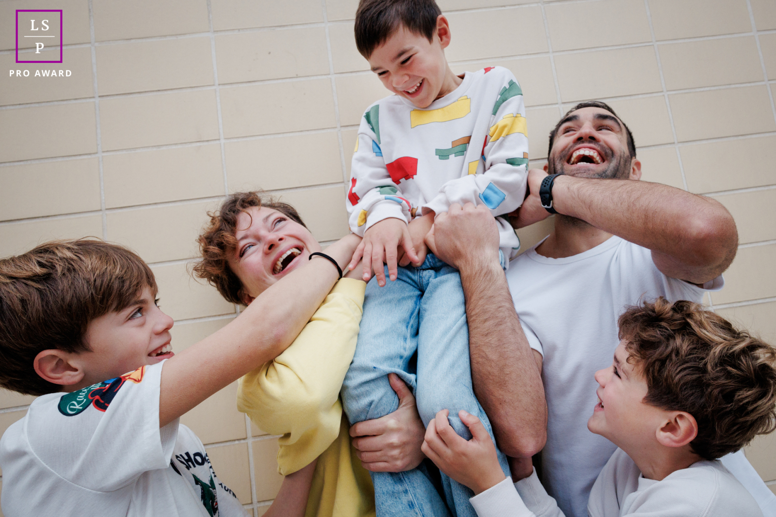 This family collapses into joyful chaos as everyone reaches toward the laughing child lifted above the group. The tight framing and overlapping hands amplify the energy, turning this playful moment into a portrait overflowing with movement and humor