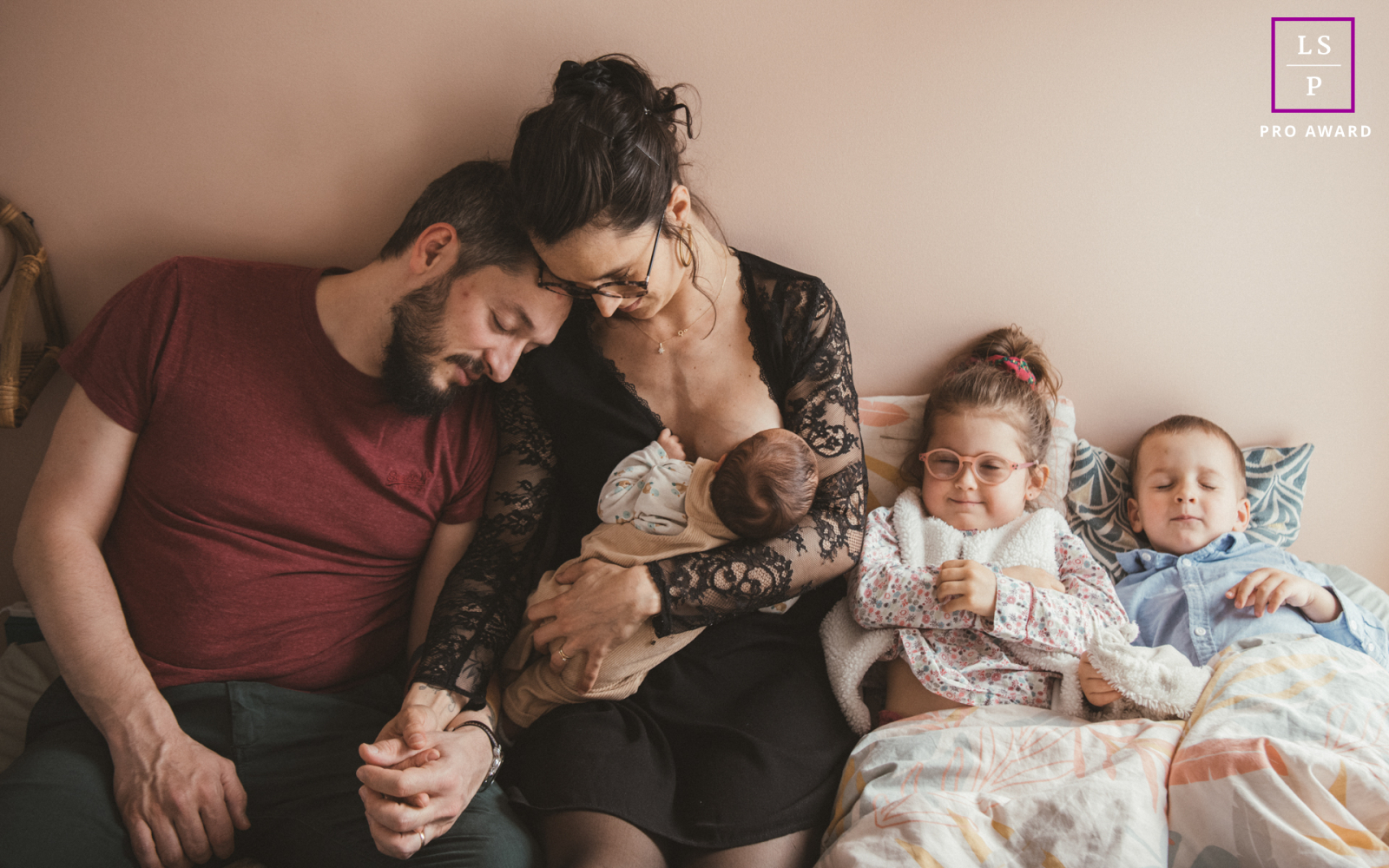 This intimate domestic tableau captures the quiet exhaustion and profound beauty of a growing family, layering the mother’s nurturing focus against the father’s weary lean. It is a masterfully tender scene.