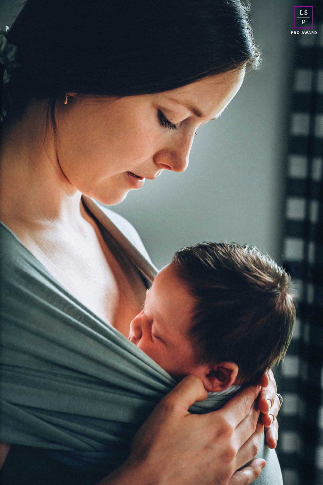 In Burnstown, a mother holds her newborn close against her chest with quiet protectiveness and calm focus. The soft directional light and intimate framing give the photograph warmth, tenderness, and the deep comfort of early connection.