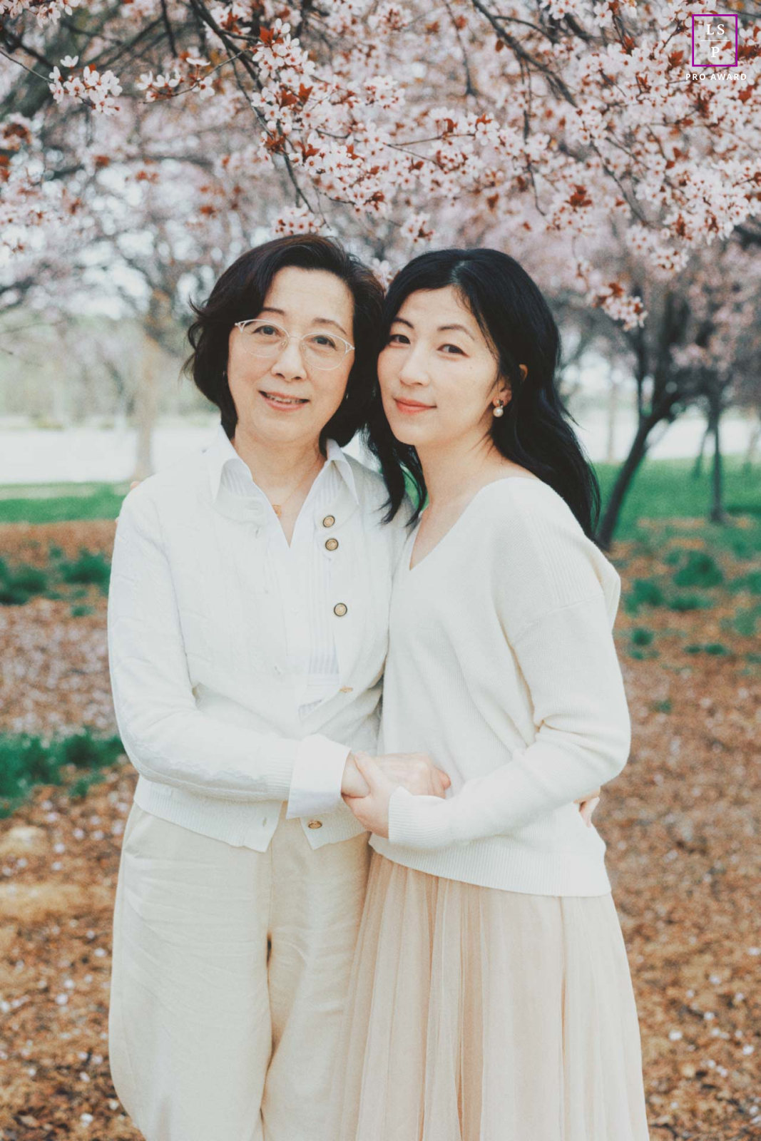 In San Ramon, CA, the mother and daughter stand closely beneath blooming trees, their matching expressions and soft tones reflecting a natural bond between generations. The delicate spring colors give the portrait elegance, warmth, and family connection.