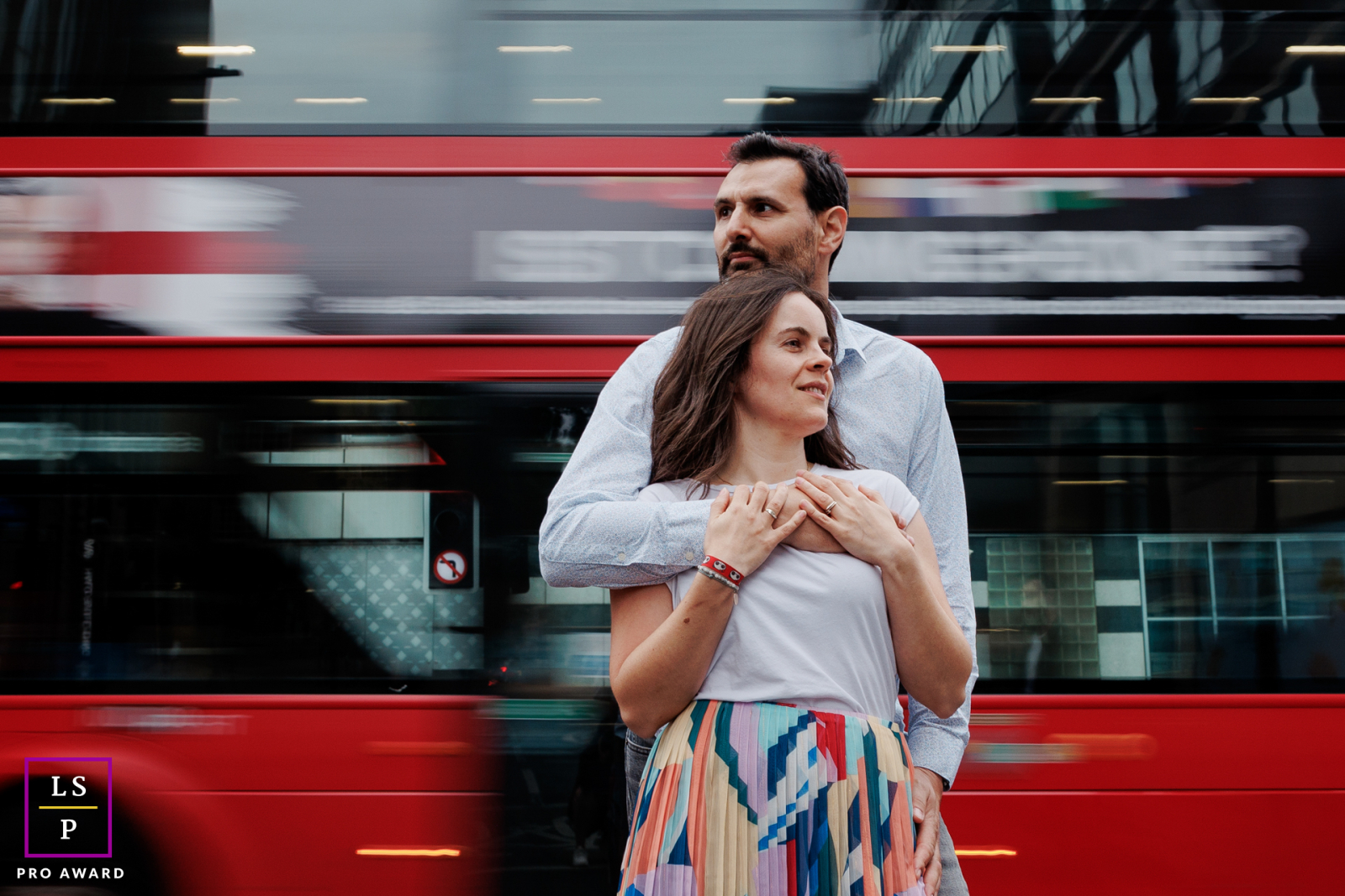 Un couple heureux s'embrasse dans les rues animées de Londres, avec un bus rouge flou en arrière-plan, créant une scène urbaine dynamique.