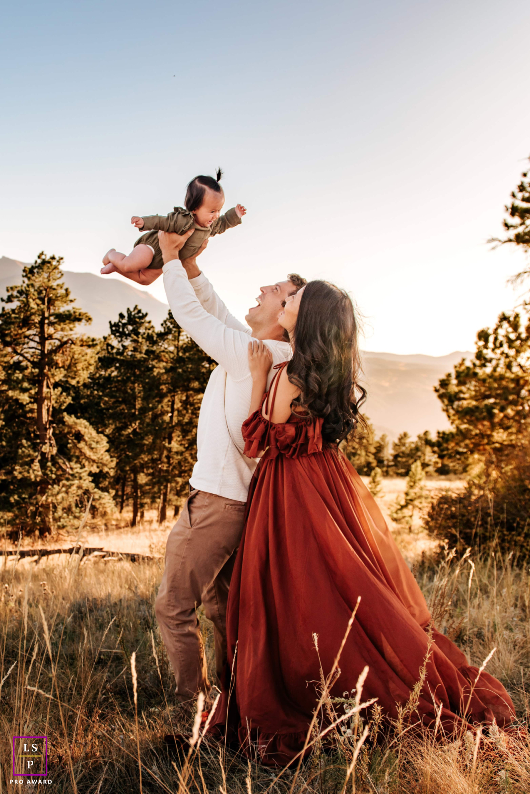 In Colorado, a dad joyfully lifts his daughter into the air while the mom stands close by, all enjoying a beautiful day in nature.