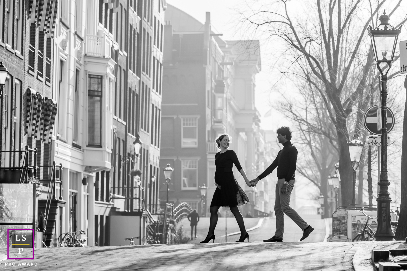 On a foggy Amsterdam morning near Magere Brug, this couple walks through the quiet street carrying the invisible anticipation of their first child. The black and white tones, soft haze, and elegant spacing create an image with tenderness and mystery.