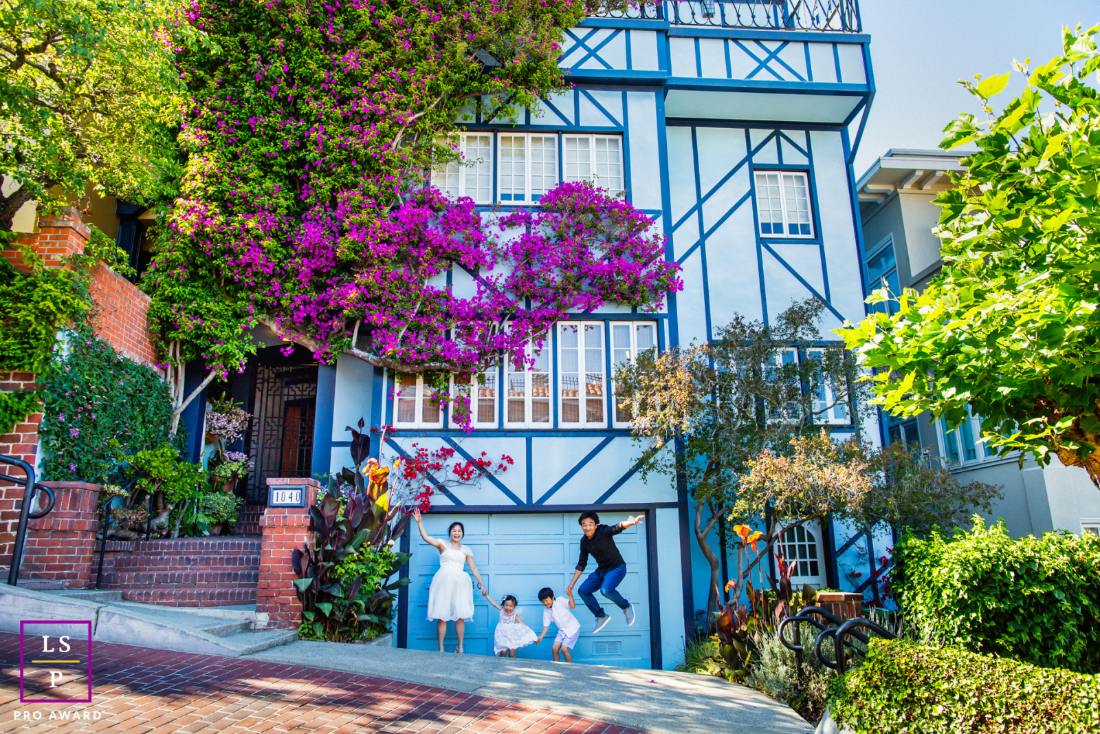 Set against the colorful hillside architecture of San Francisco, this playful family scene turns an ordinary driveway into a stage for imagination. The vibrant flowers, bold blue house, and perfectly timed jump give the photograph energy, humor, and charm
