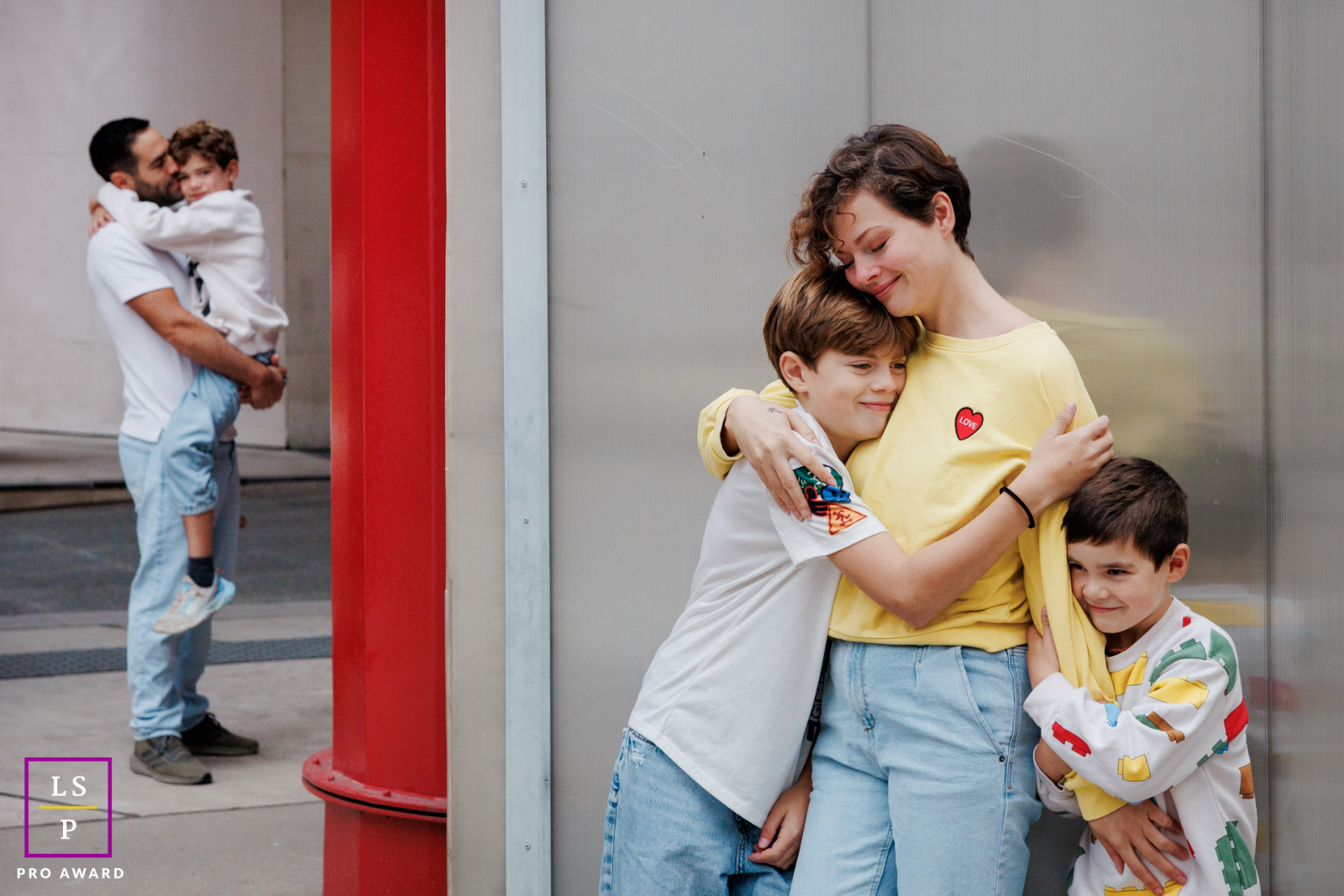 In Paris, the family spreads naturally across the frame as the children cling affectionately to their mother while the father holds another child in the distance. The layered composition and soft reflections create a portrait filled with warmth.