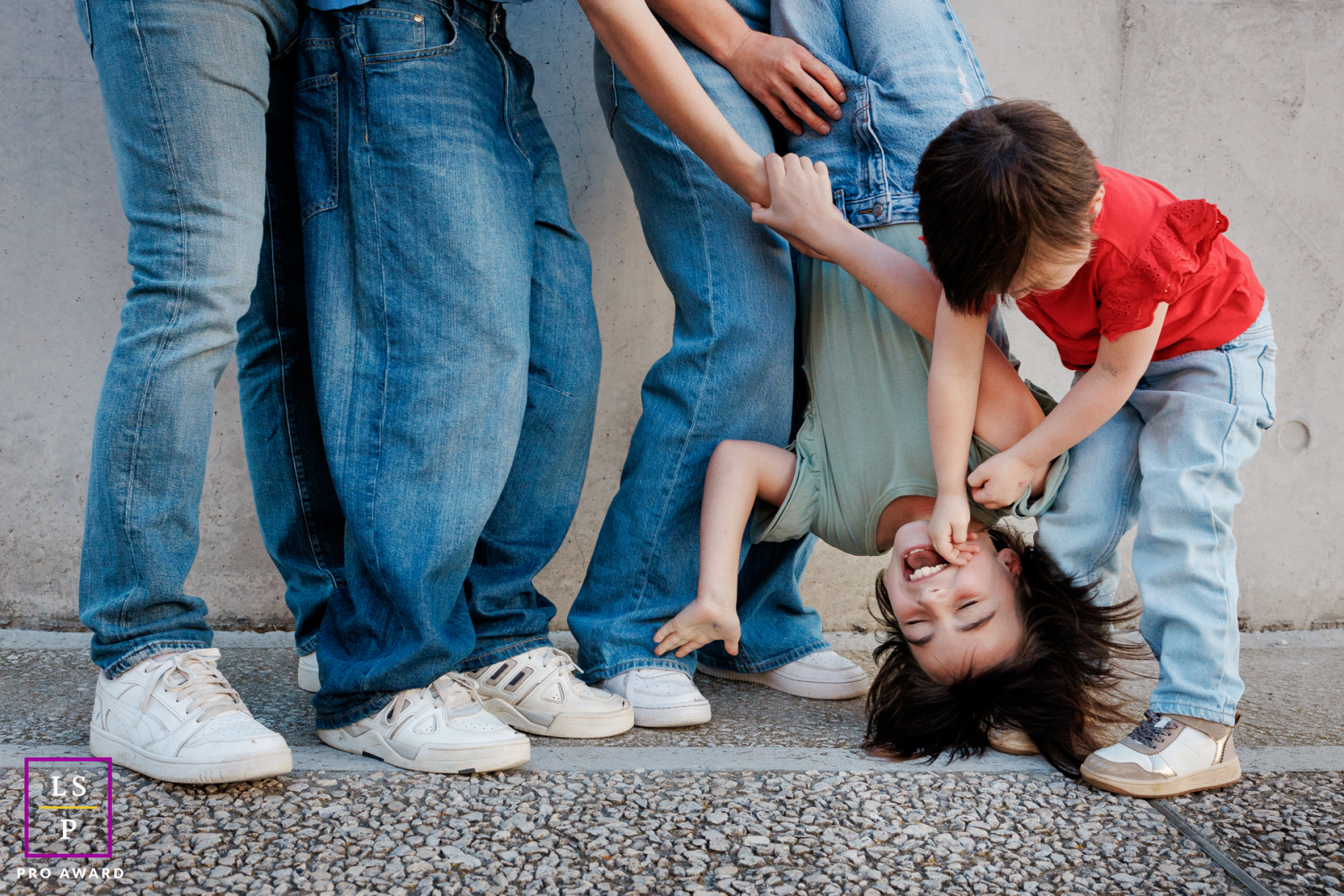 In Paris, the family dissolves into laughter as the older sister hangs upside down between her parents while her younger brother joins the chaos. Cropped framing and playful movement turn this family portrait into something wonderfully energetic.