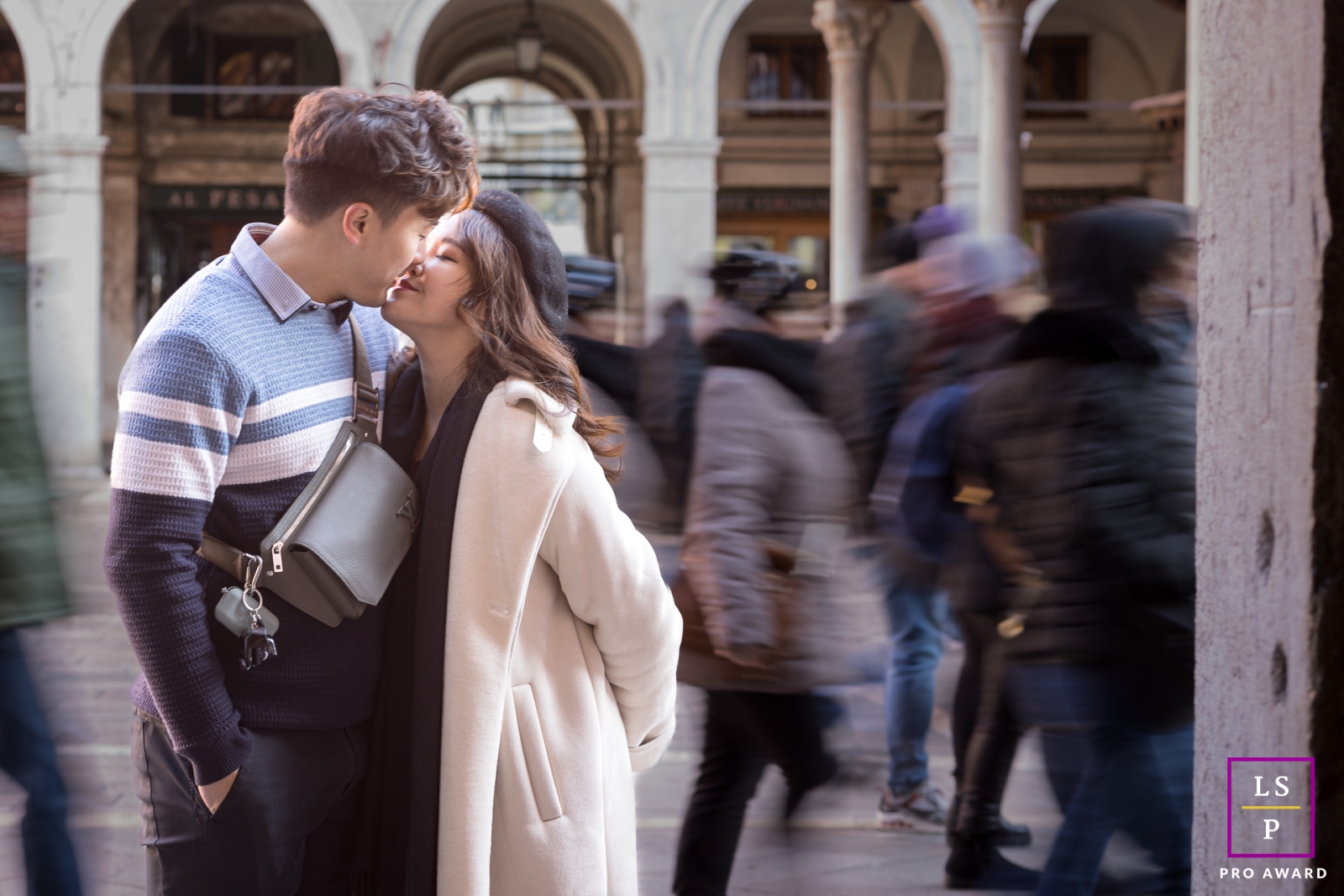 In a captivating lifestyle portrait, a couple poses against the backdrop of a Venetian holiday, with the vibrant movement of pedestrians