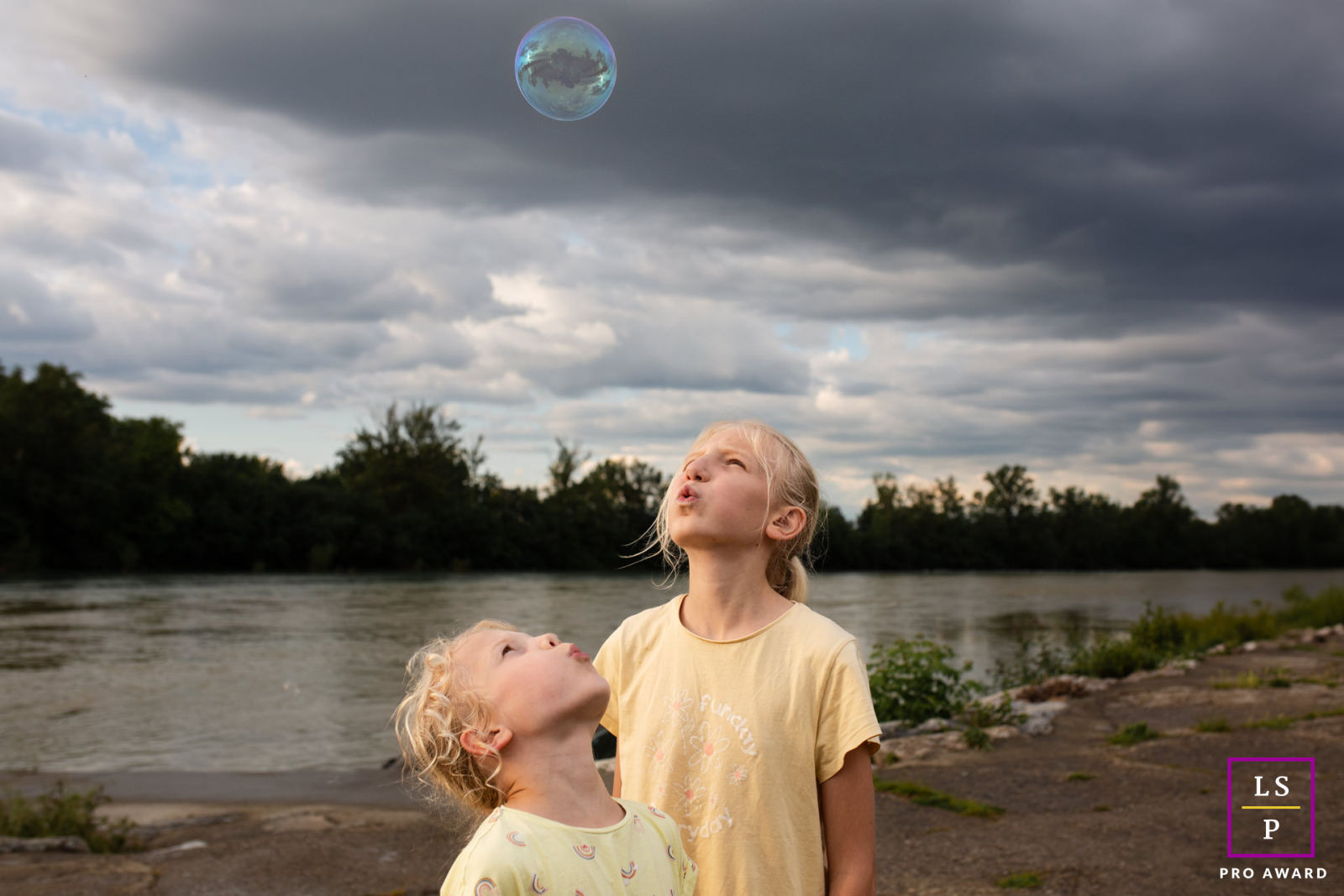 In Haute-Garonne, siblings are looking up at a floating soap bubble. The portrait captures the children's innocent and joyful fascination.