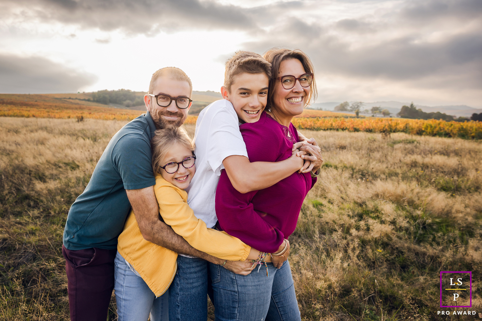 In the open countryside near Lyon, this family squeezes together so tightly they resemble one joyful human sandwich. The playful stacking of arms, smiles, and faces gives the photograph humor, warmth, and wonderfully unfiltered family affection.