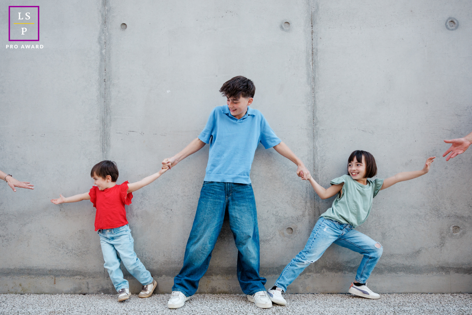 In Paris, the siblings turn a simple game into family comedy as the brother keeps his sisters from choosing sides between their parents. The outstretched arms and clean backdrop give the portrait playful tension and irresistible humor.