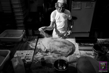 In Cauneille, the baker works beneath dramatic light as flour falls across an enormous mound of dough. The overhead perspective reveals the beautiful chaos of the workspace, turning an ordinary baking routine into something cinematic and hardworking.