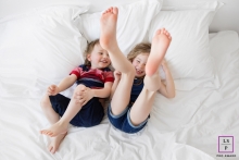 The kids were kicking and laughing while lying on a bed with white sheets, indoors at home for a lifestyle portrait Lifestyle Family Portraits in Marseille Bouches-du-Rhone - Photo contains: bed, white sheets, kids, legs, kicking, laughing, color, indoors