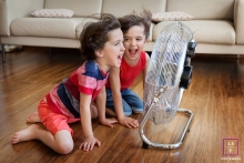 The boys were laughing with their hair blowing in the wind, facing into a blowing fan, inside on a wood floor, for a lifestyle family portrait Lifestyle Family Portrait Photography in Bouches-du-Rhone | Image contains: boys, couch, inside, wood floor, fan, laughing, hair, wind, color