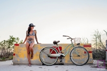 This woman exudes confidence and freedom as she poses in her swimsuit near her beach cruiser in front of a concrete barrier, creating a beautiful and fun lifestyle picture Woman Portrait Session in Key West FL | Lifestyle Photography contains: woman, swimsuit, beach cruiser, bike, concrete barrier