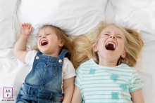 This closeup of two sisters laughing and being playful on a bed captures the spirit of fun and closeness Marseille Family Lifestyle Portrait Photography Bouches-du-Rhone | Image contains: sisters, bed, laughing, playful, fun, closeup