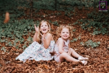 As irmãs da Alsácia sentam e brincam nas folhas caídas juntas sob as árvores em Grand Est
