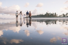 A family walks together, holding hands, as they cross over a serene reflecting pool on the beautiful beach in Maceio