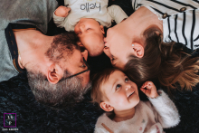 An image was taken in Annecy, Haute-Savoie, France, showing a family of 4 with a newborn on their backs, in a circle, captured in a relaxed and natural setting.