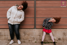A lifestyle image created at Frangy, Haute-Savoie, France shows a mom and daughter happily shaking their heads as they share a laugh during a portrait session capturing their special bond.