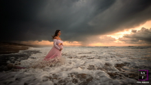 A glowing mother-to-be stands fearlessly against a stunning backdrop of a moody sky and powerful ocean, symbolizing her strength and beauty during pregnancy.