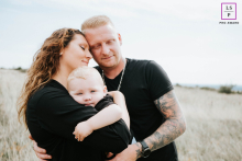 Um abraço terno na natureza, enquanto uma família de três pessoas, vestida de preto, aproveita a beleza de seu vínculo em Colmar.